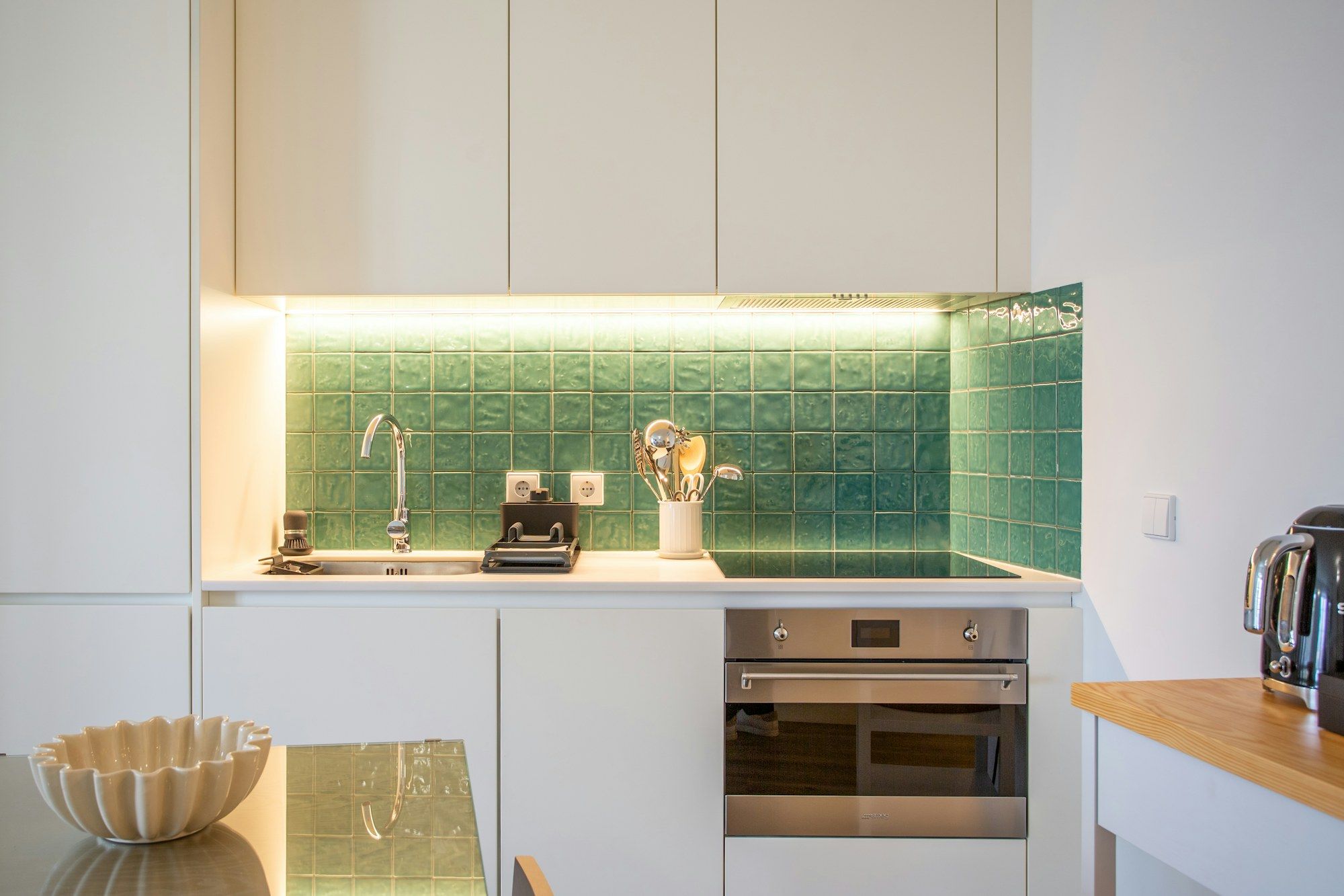 Kitchen with green tiles, an oven and warm under-cabinet light