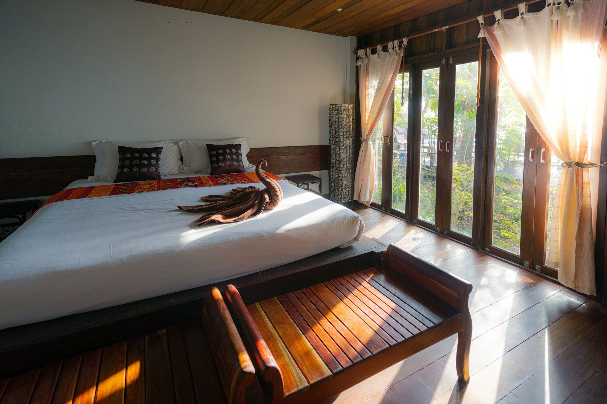 Bed in morning sun with a wooden bench at its foot